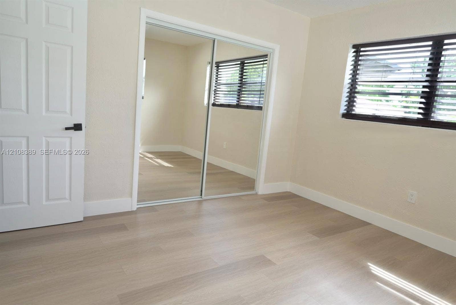 Room featuring wood-finish flooring, sliding mirror-panel closet doors, and horizontal window blinds with matte black hardware