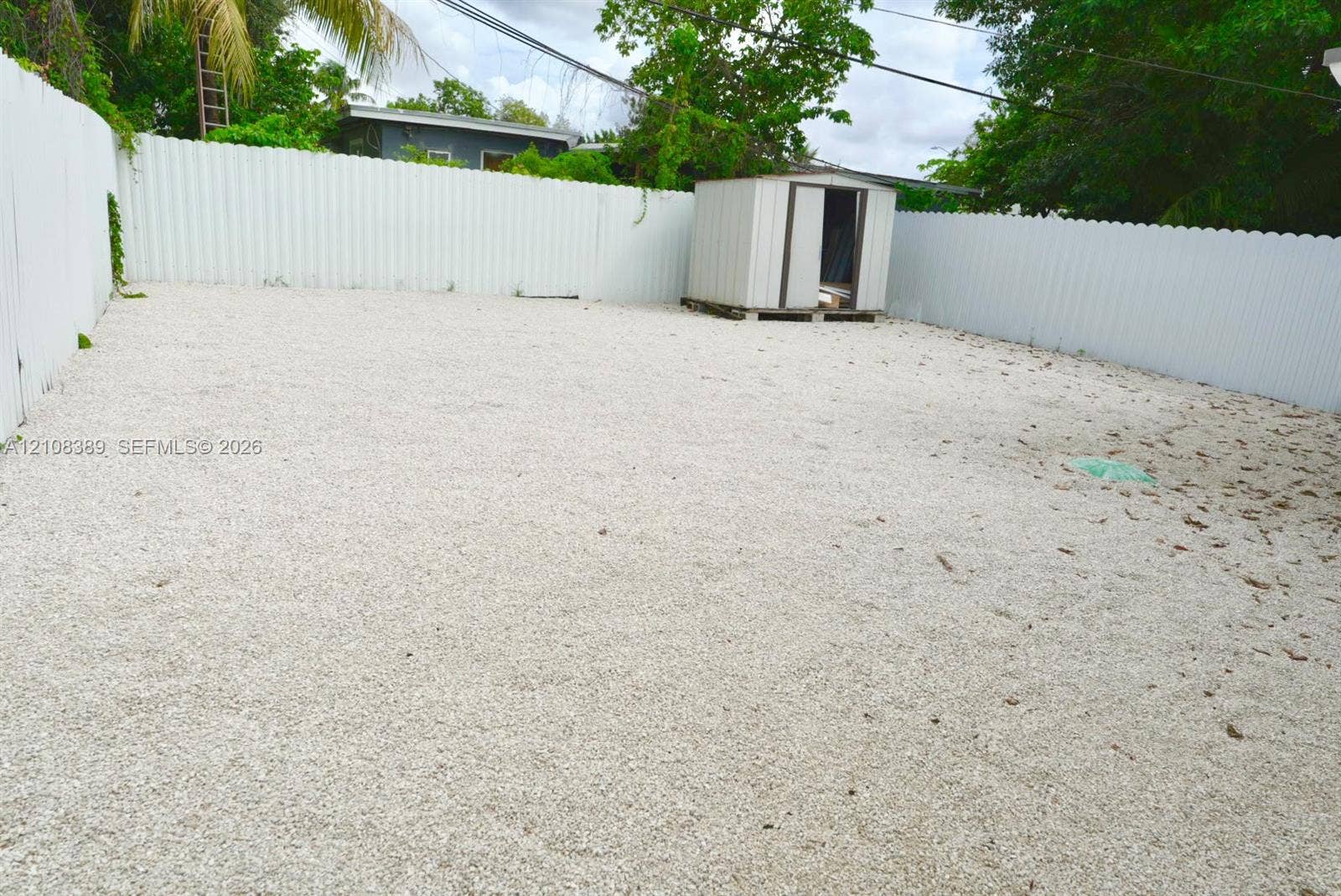 Fenced backyard featuring white gravel ground cover and a detached storage structure