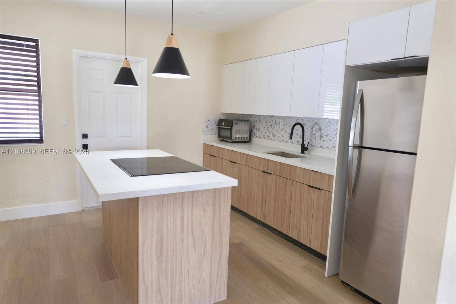 Kitchen featuring a central island with a solid surface countertop and integrated cooktop, wood-finish cabinetry, white high-gloss upper cabinets, patterned backsplash, and matte black pendant lighting