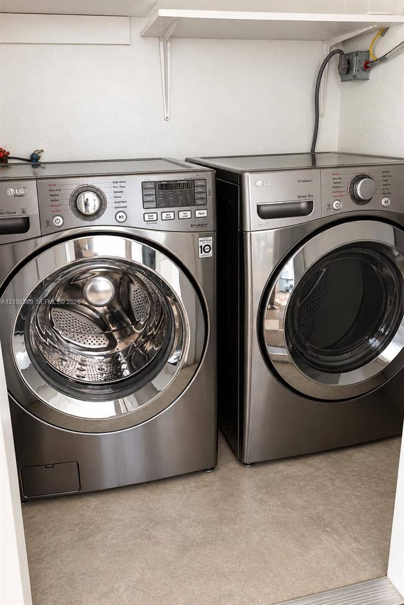 Laundry area featuring stainless steel front-load washer and dryer set, installed wall-mounted metal shelving, and neutral flooring