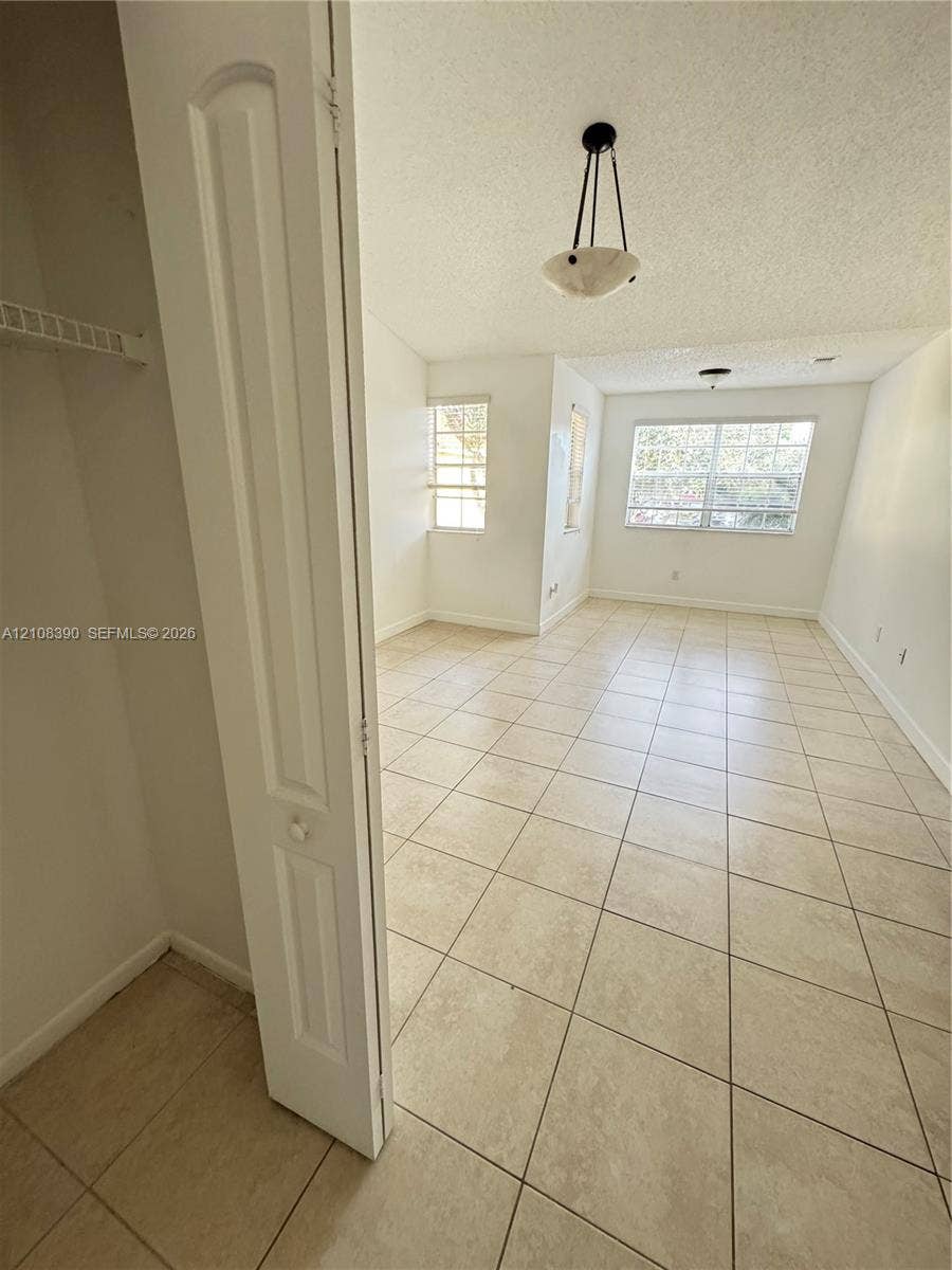 18346 NW 68th Avenue, #K, Hialeah, Hialeah, FL 33015 Interior space featuring large-format ceramic tile flooring, neutral walls, multi-pane windows, a built-in closet with bifold doors, and an overhead pendant light fixture