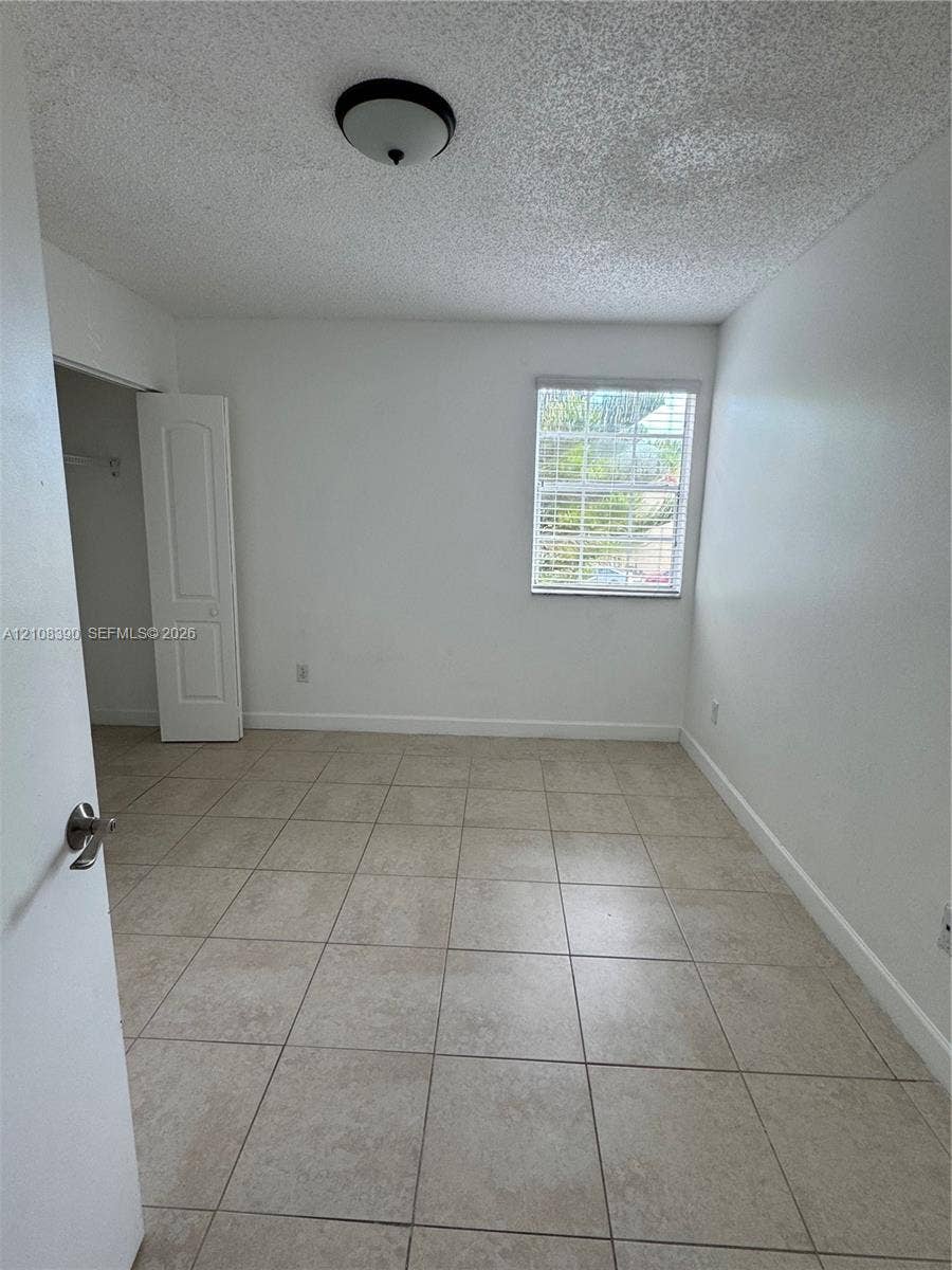 18346 NW 68th Avenue, #K, Hialeah, Hialeah, FL 33015 Room featuring neutral-tone tile flooring, a single-panel interior door, a built-in closet, and a window with horizontal blinds