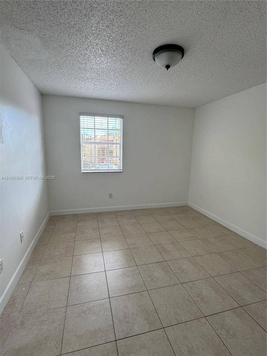 18346 NW 68th Avenue, #K, Hialeah, Hialeah, FL 33015 Interior space featuring large-format ceramic tile flooring, neutral wall tones, a single-pane window with internal grids, and a central dome-style ceiling light fixture
