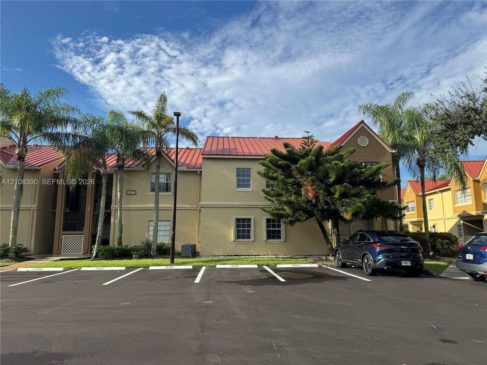 18346 NW 68th Avenue, #K, Hialeah, Hialeah, FL 33015 Multi-story stucco exterior featuring a red metal roof, decorative gable trim, and paved surface parking