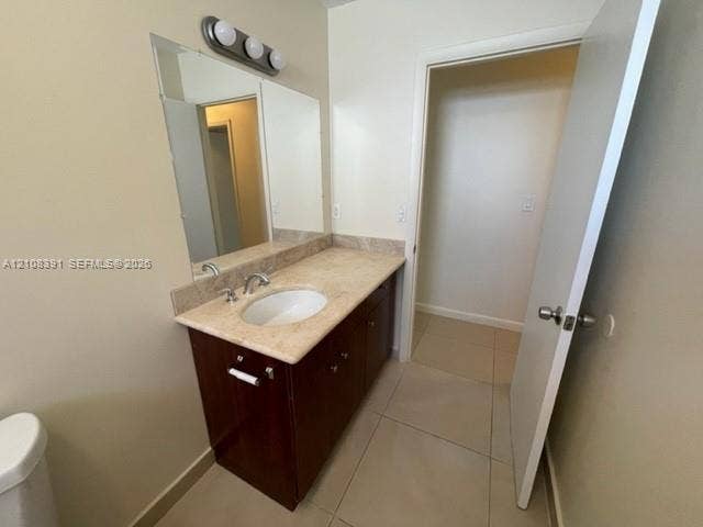 18233 Oleta Drive, #18233, North Miami Beach, North Miami Beach, FL 33160 Vanity featuring a stone countertop with an integrated basin, wood-finish cabinetry, a large wall-mounted mirror, three-light fixture, and neutral tile flooring