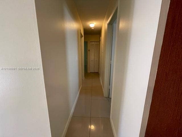 18233 Oleta Drive, #18233, North Miami Beach, North Miami Beach, FL 33160 Interior hallway featuring neutral-toned tile flooring, smooth wall finishes, and bifold closet doors