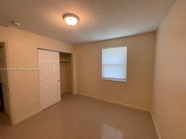 18233 Oleta Drive, #18233, North Miami Beach, North Miami Beach, FL 33160 Neutral-toned interior space featuring light-colored tile flooring, a single window with blinds, and a built-in closet with panel doors