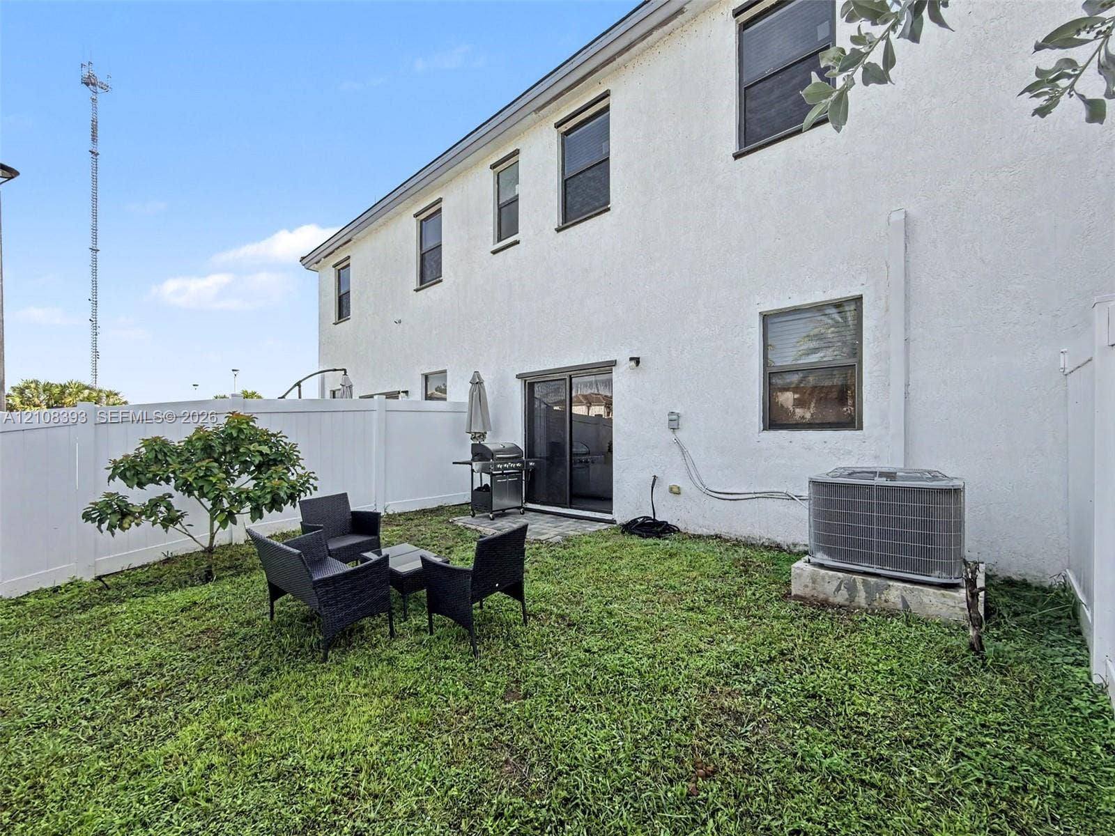 Stucco exterior featuring dual-story construction, sliding glass entry doors, and a white vinyl privacy fence enclosing the backyard