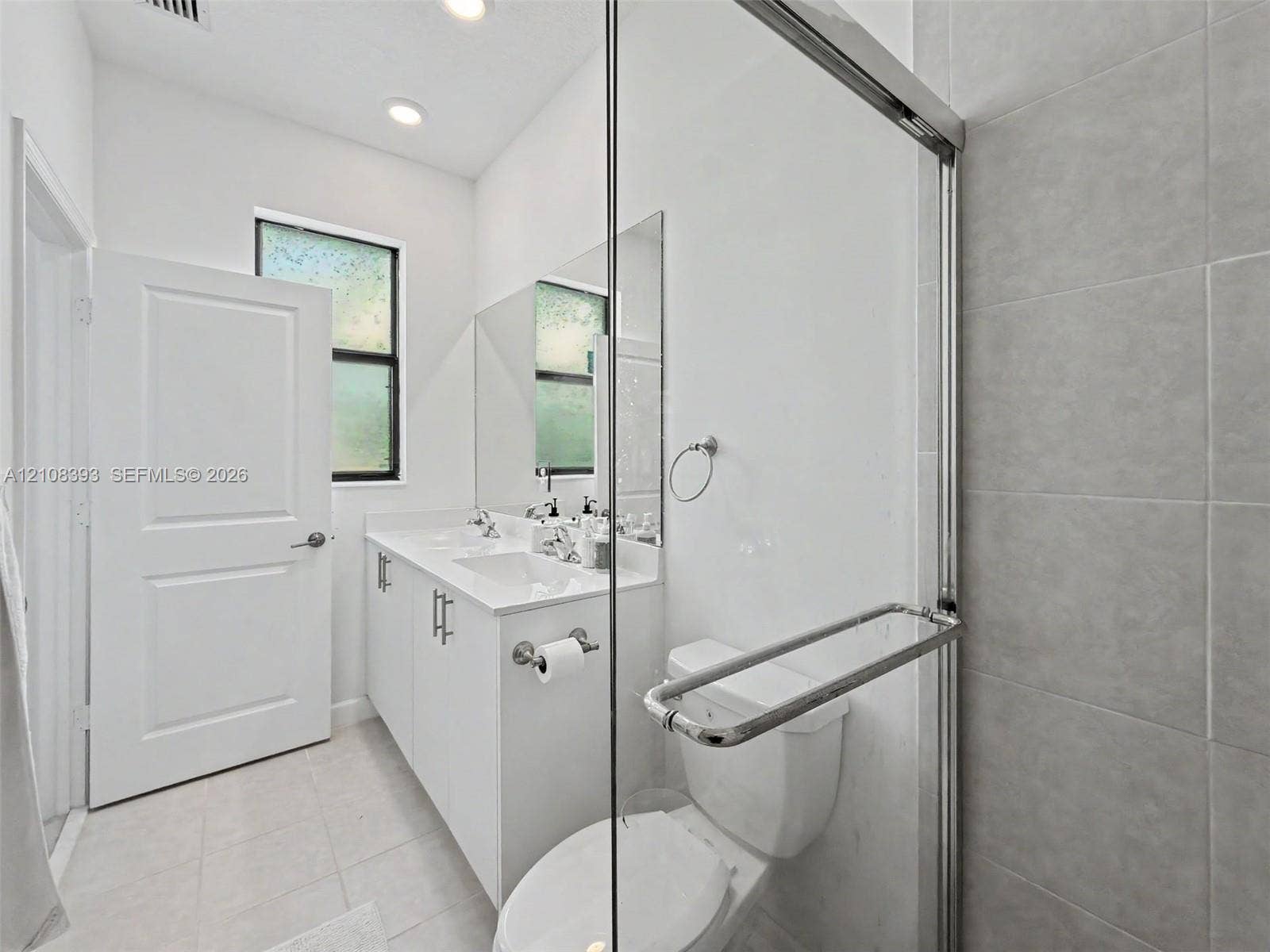 Double vanity with integrated sinks, white cabinetry, polished chrome hardware, and glass-enclosed shower with large-format tile surround