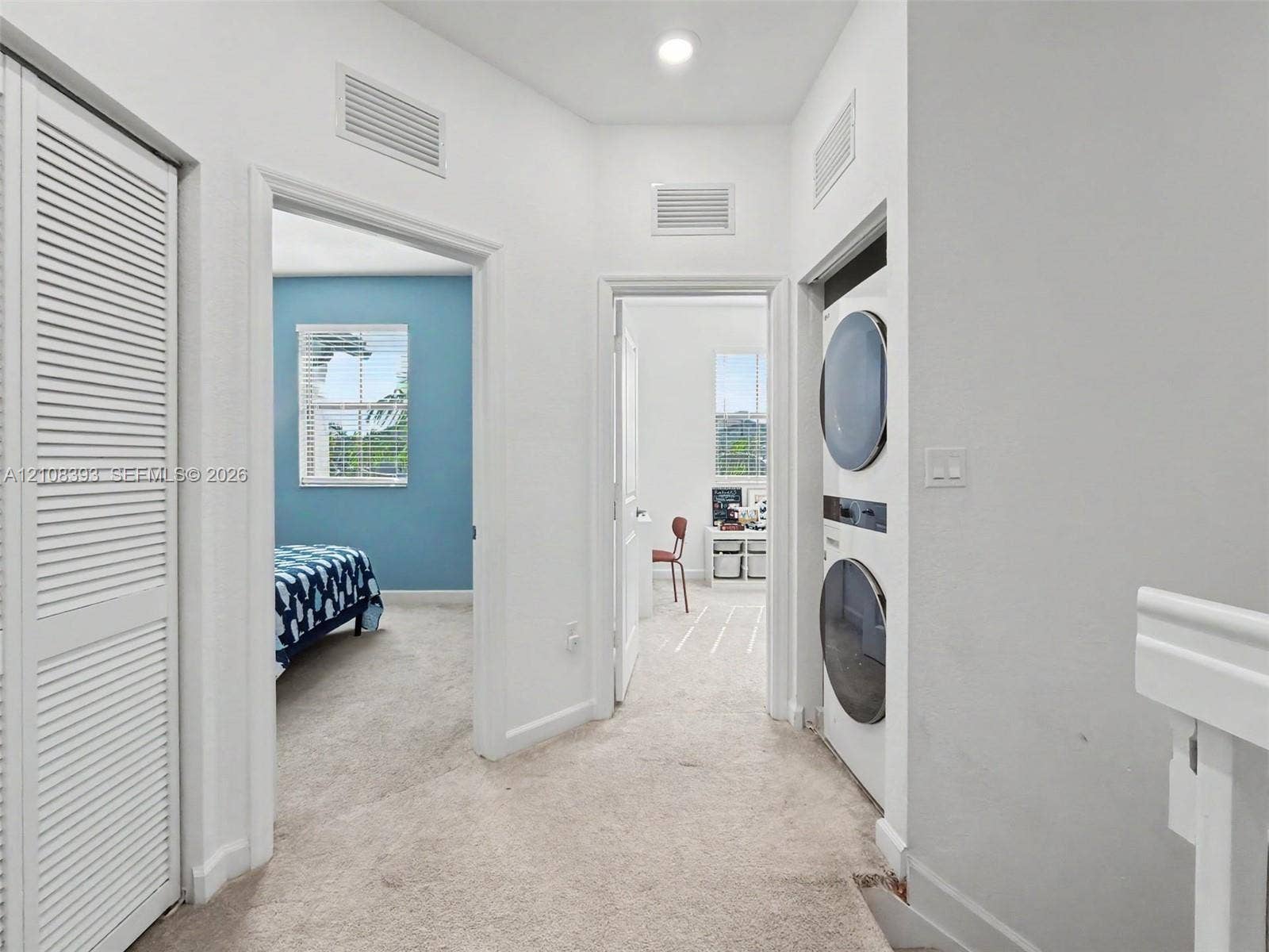 Hallway featuring neutral carpeting, a built-in stacked laundry unit, and louvered closet doors