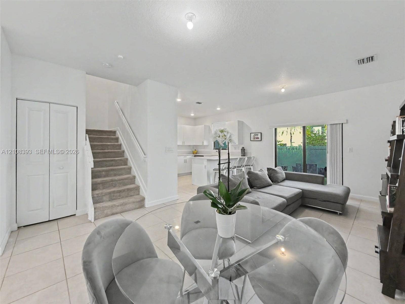 Open-concept interior featuring neutral tile flooring, recessed lighting, carpeted staircase with white balusters, white cabinetry, and sliding glass doors