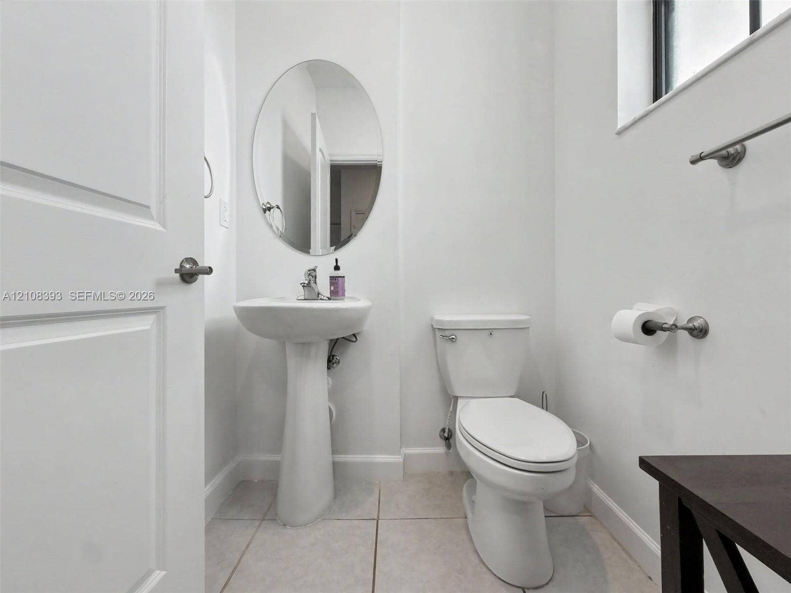 Pedestal sink, oval wall mirror, ceramic tile flooring, and a two-piece toilet