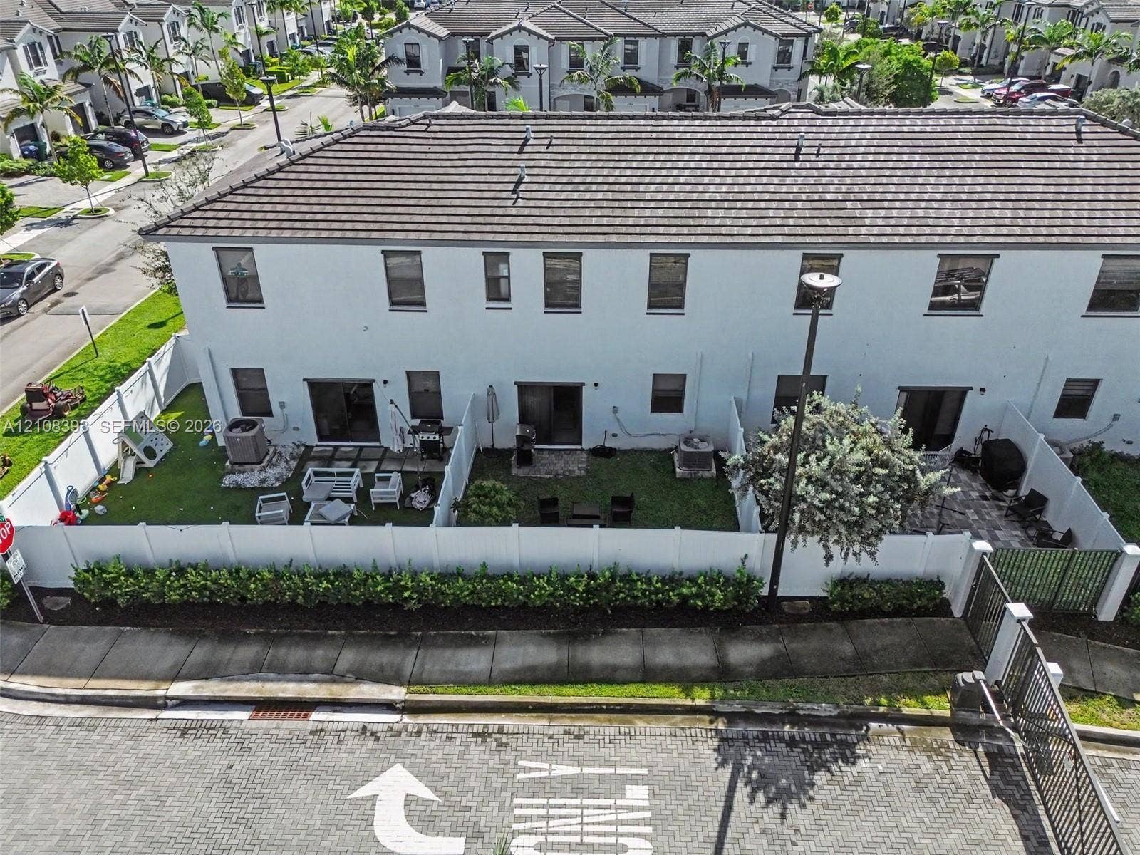 Two-story townhouse exterior featuring white stucco siding, a tiled roof, private fenced rear yards with patio pavers, and manicured landscaping