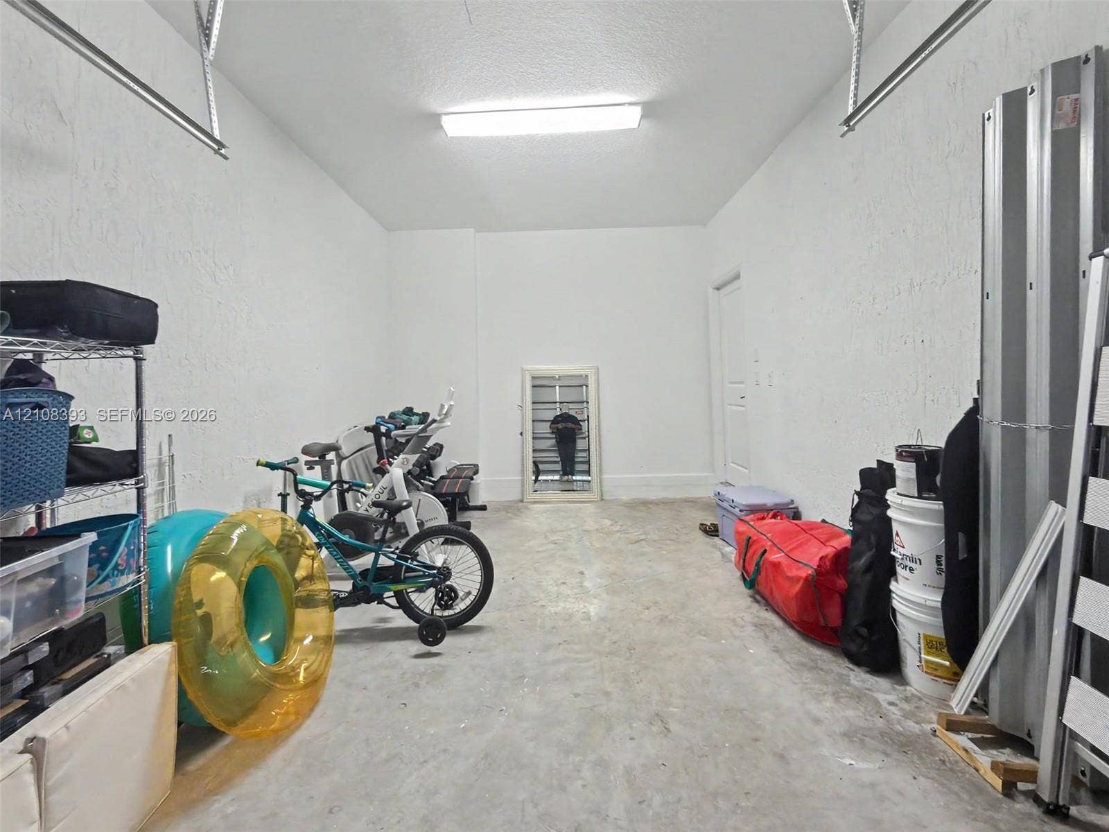 Enclosed garage featuring concrete flooring, textured walls, and overhead LED lighting