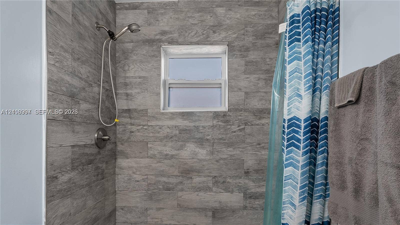 Shower enclosure featuring wood-finish wall tile, a single-handle faucet, a handheld showerhead, and a rectangular window