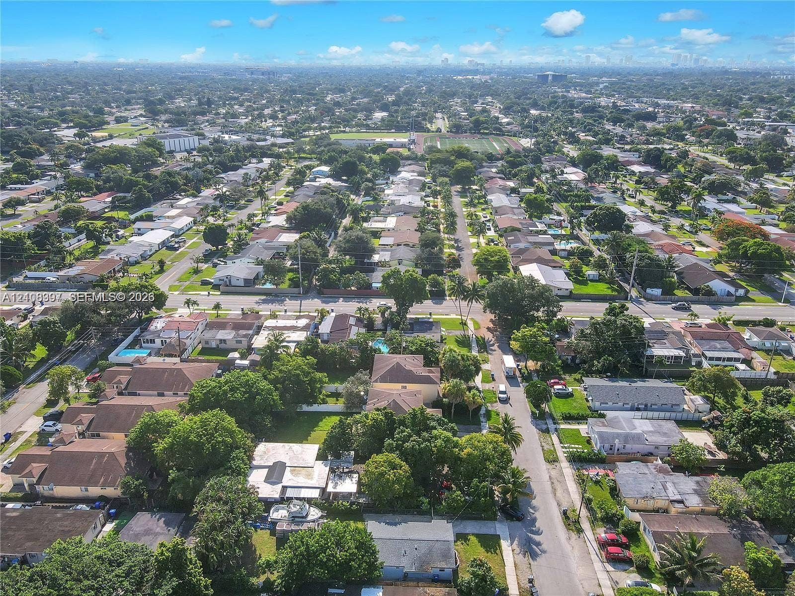 Aerial perspective of a residential neighborhood featuring paved streets, established tree canopy, diverse housing styles, and proximity to open green space