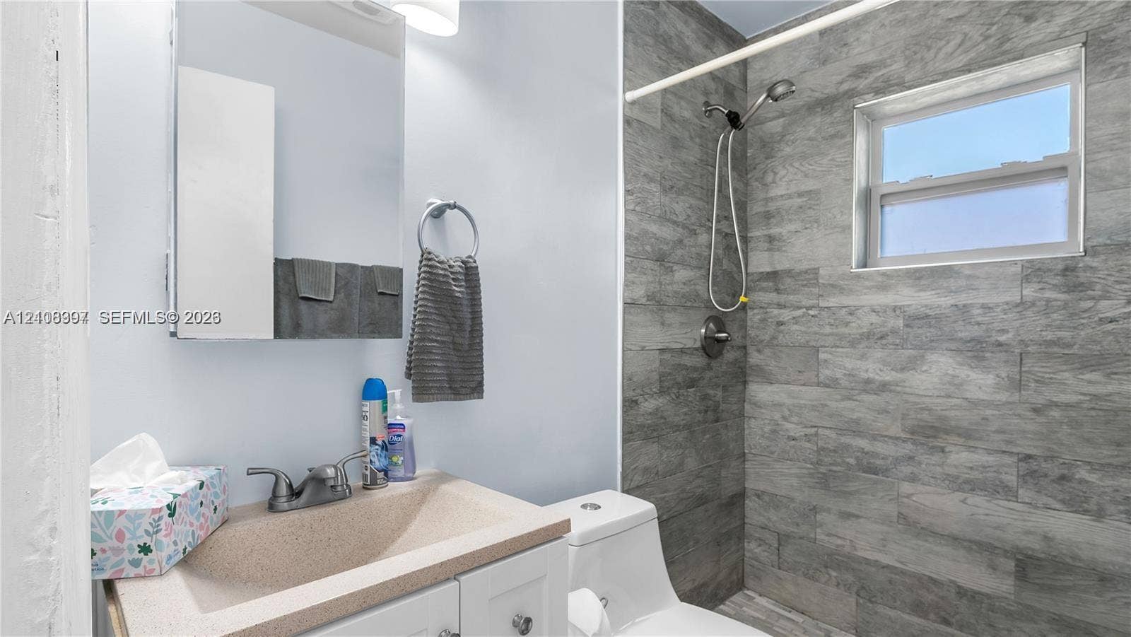 Bathroom featuring a vanity with integrated sink, wall-mounted medicine cabinet, shower area with wood-finish tile surround, and a single-hung window