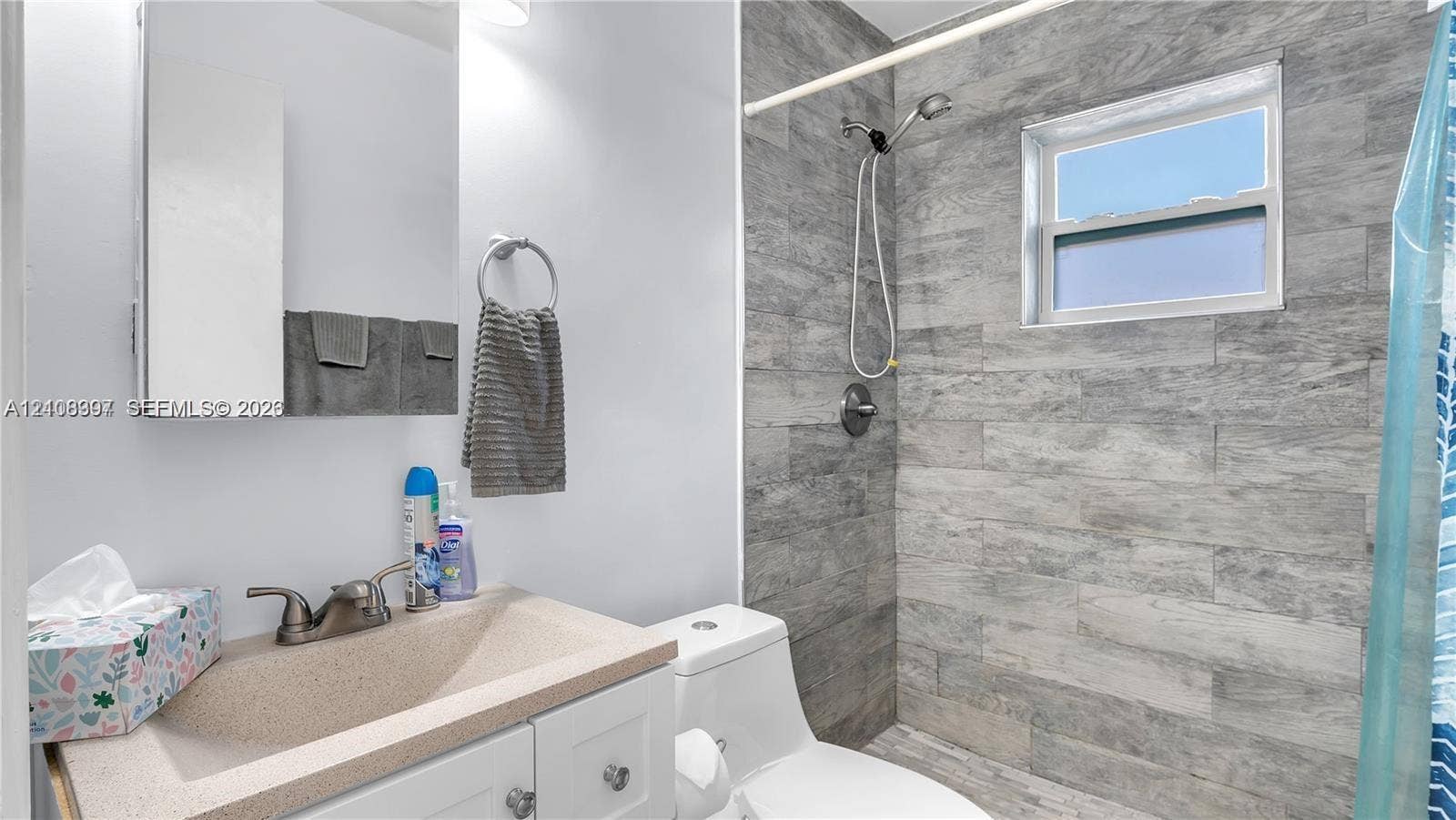 Bathroom featuring a vanity with an integrated basin, a wall-mounted mirrored medicine cabinet, a shower enclosure with horizontal-plank tile wall surfacing, a hand-held shower fixture, and a single-hung window