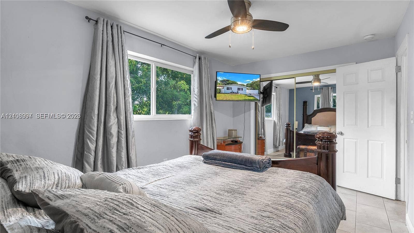 Bedroom featuring large windows with natural light, mirrored sliding closet doors, ceramic tile flooring, and a ceiling fan with integrated lighting