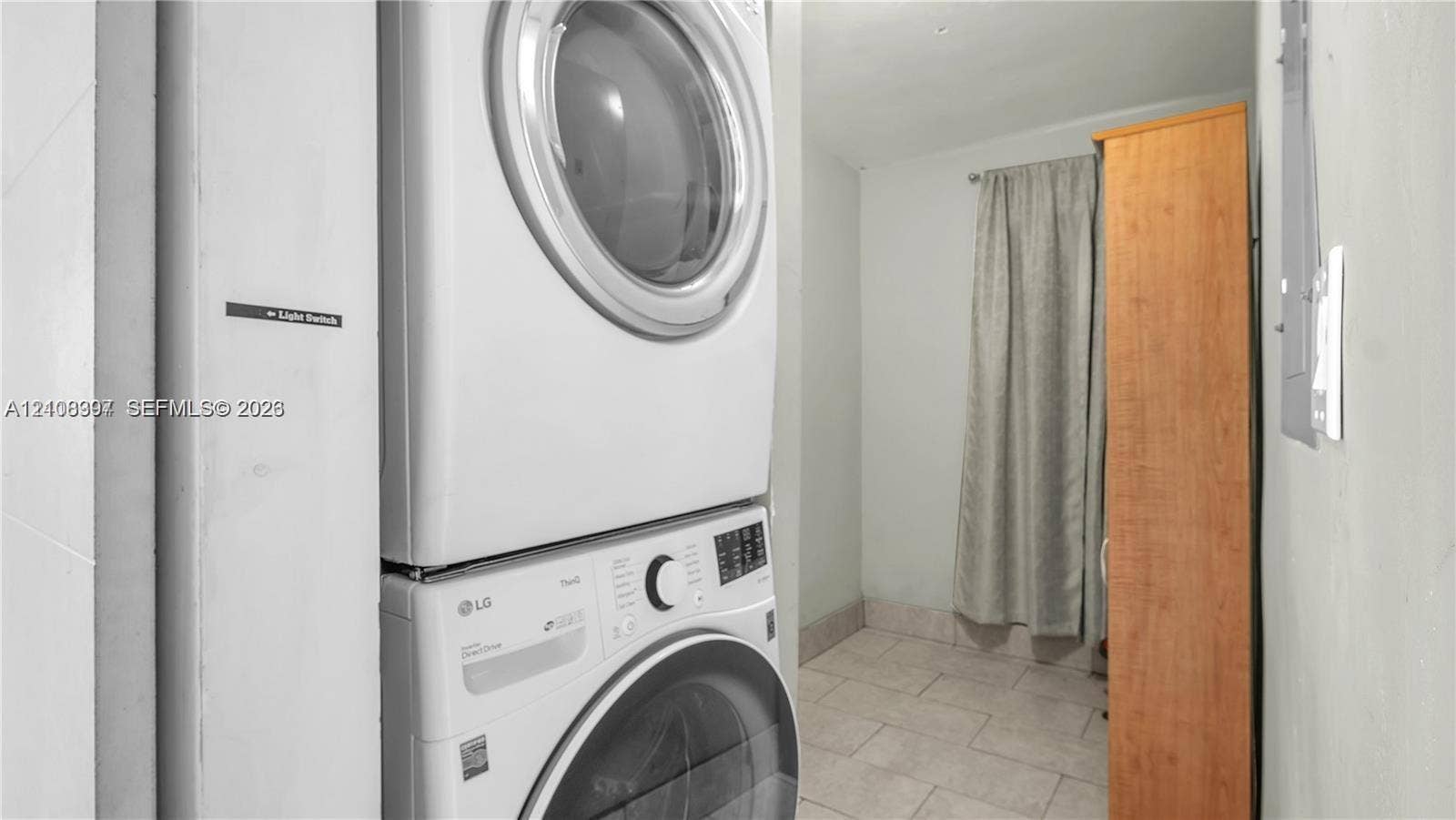 Stacked laundry unit featuring a white front-load washer and dryer with light-toned ceramic tile flooring