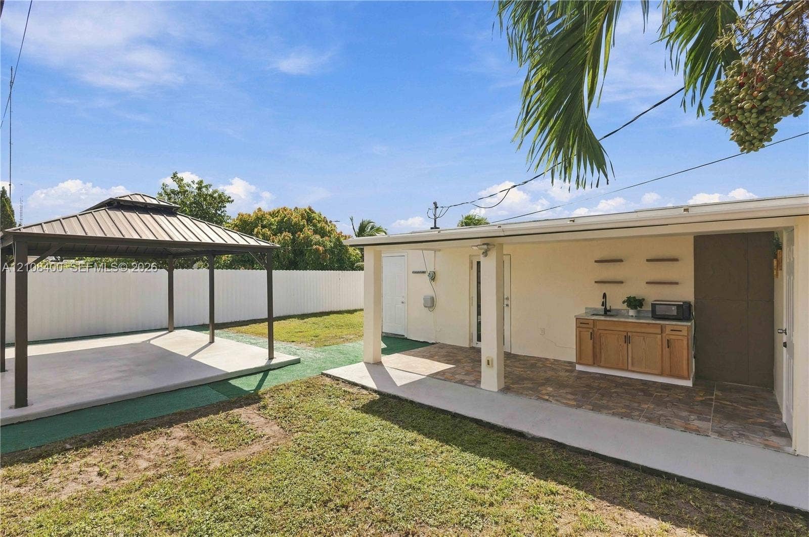 2551 SW 53rd Avenue, West Park, West Park, FL 33023 Backyard featuring a detached metal-frame gazebo with a concrete pad, a covered patio with tile flooring, and an outdoor kitchenette with wood-finish cabinetry and a stone-surface countertop