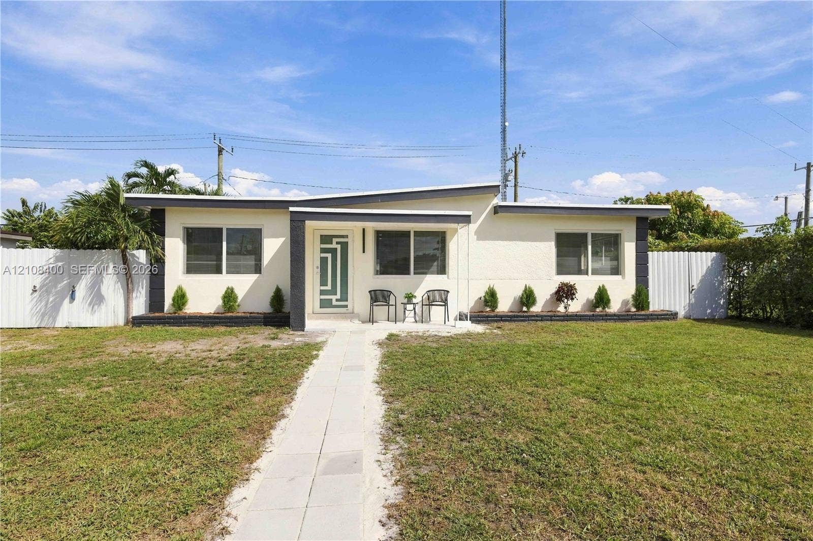 2551 SW 53rd Avenue, West Park, West Park, FL 33023 Mid-century modern exterior featuring a low-slope roofline, light-colored stucco facade, geometric-patterned entry door, and white privacy fencing