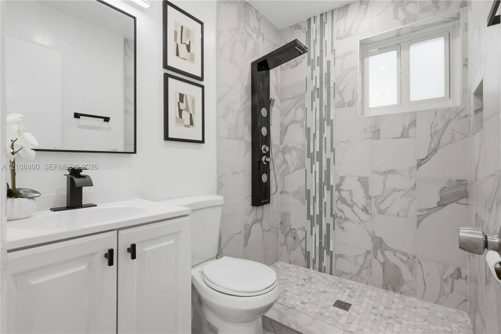 2551 SW 53rd Avenue, West Park, West Park, FL 33023 Bathroom featuring large-format wall tile, shower panel system with integrated body jets, walk-in shower with pebble tile flooring, vanity with matte black faucet hardware, and a framed mirror