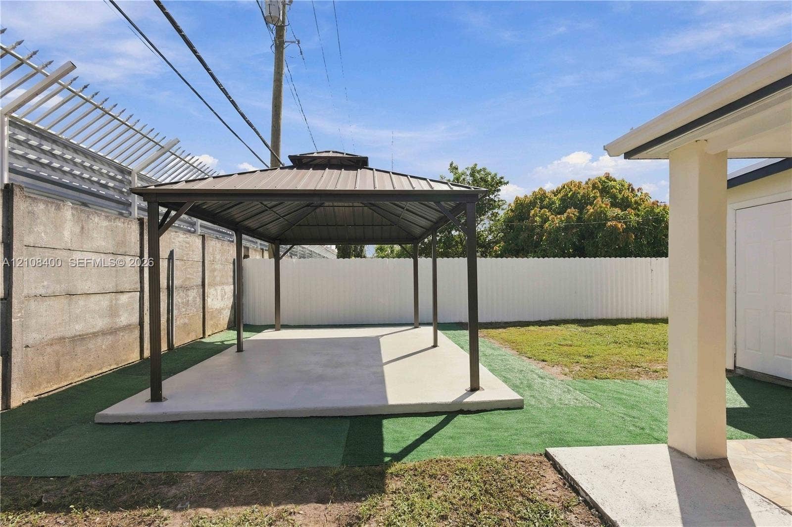 2551 SW 53rd Avenue, West Park, West Park, FL 33023 Outdoor area featuring a permanent metal-roofed gazebo, concrete foundation pad, synthetic turf surfacing, and enclosed fencing