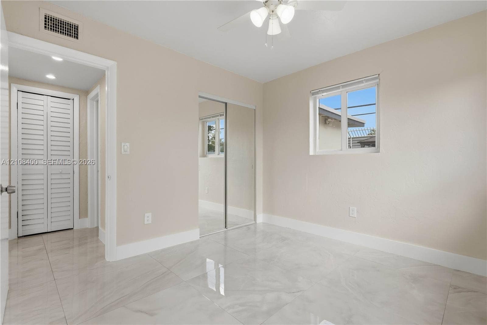 2551 SW 53rd Avenue, West Park, West Park, FL 33023 Neutral-toned room featuring large-format tile flooring, mirrored sliding-door closet, multi-pane window, and integrated ceiling fan