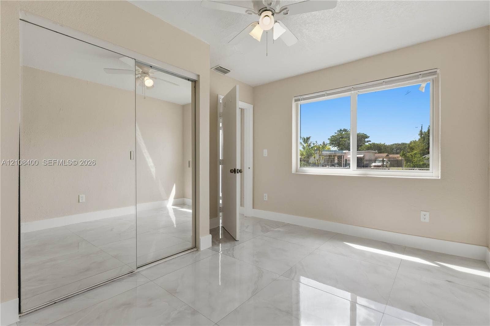 2551 SW 53rd Avenue, West Park, West Park, FL 33023 Room with high-gloss polished tile flooring, mirrored sliding closet doors, a neutral color palette, a multi-light ceiling fan, and a large horizontal window