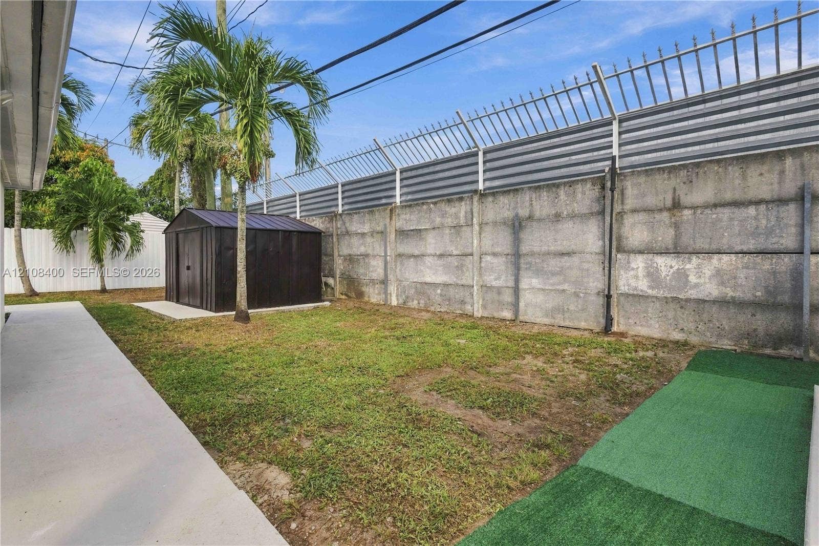 2551 SW 53rd Avenue, West Park, West Park, FL 33023 Backyard featuring concrete slab surfacing, a metal storage shed, synthetic turf sections, and a concrete perimeter wall with an integrated metal fence topper