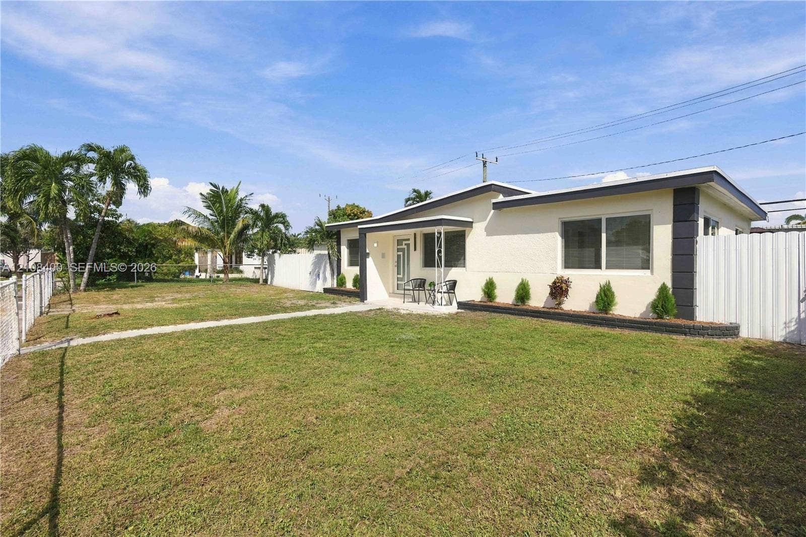 2551 SW 53rd Avenue, West Park, West Park, FL 33023 Single-story exterior featuring a light-toned textured facade, horizontal sliding windows, metal-post entryway canopy, and a fenced yard with perimeter landscaping