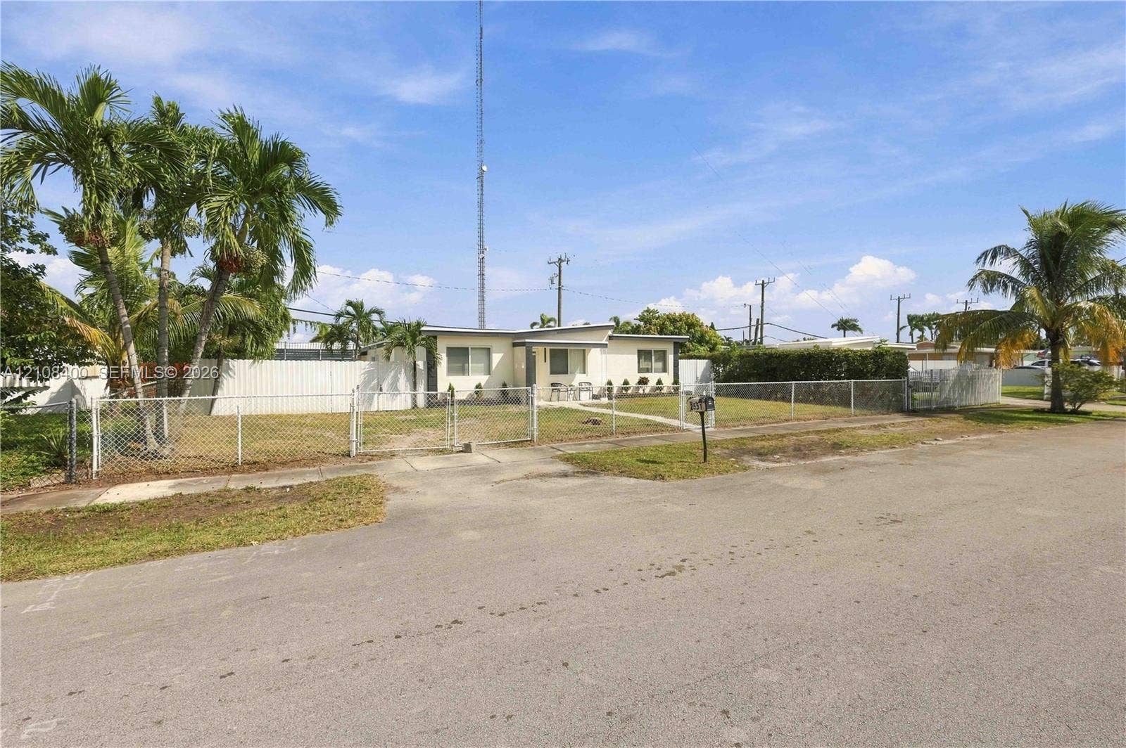 2551 SW 53rd Avenue, West Park, West Park, FL 33023 Single-story exterior featuring a stucco facade, chain-link fencing, mature palm trees, and an asphalt driveway