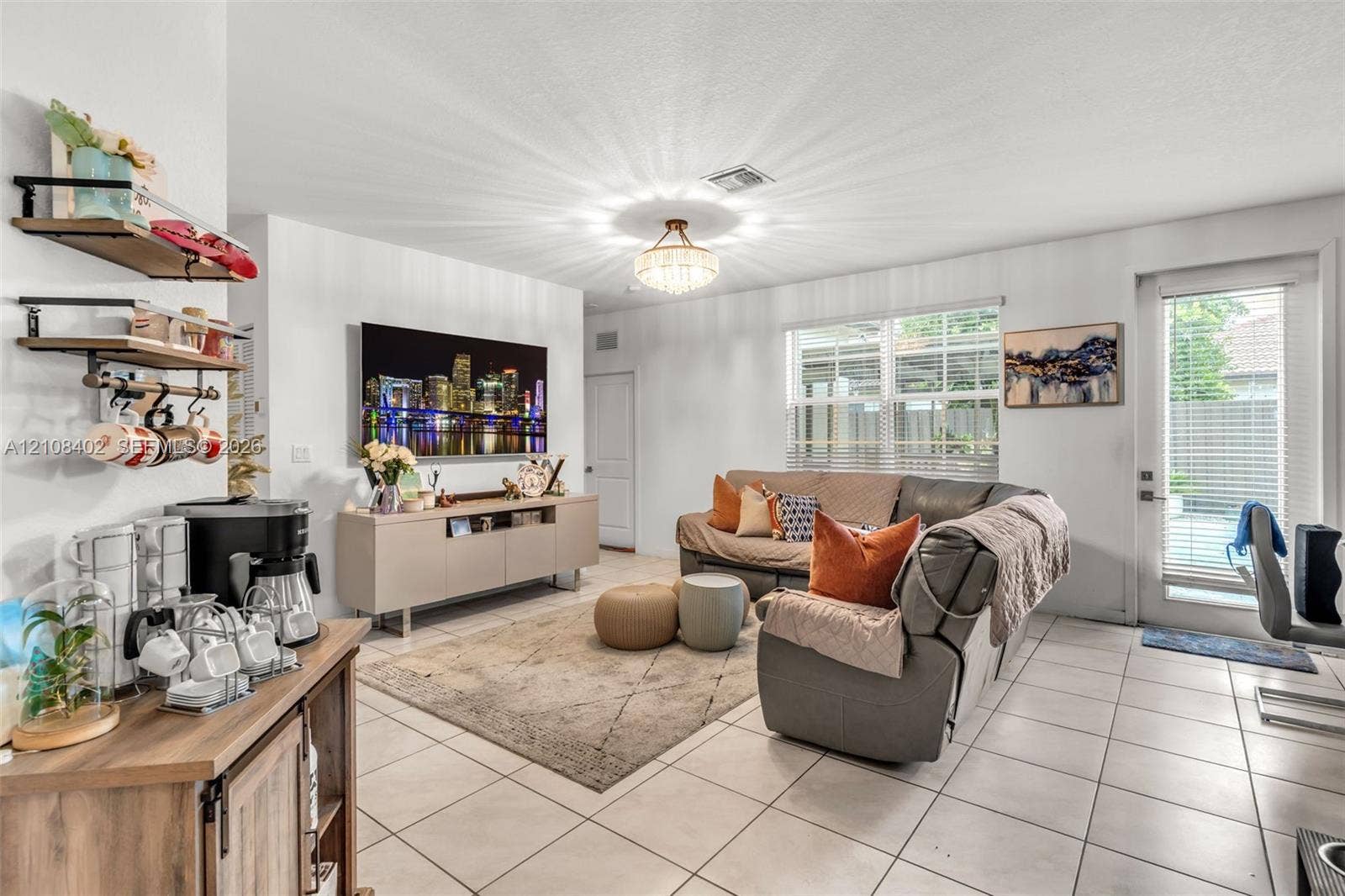 11771 SW 243rd Street, Homestead, FL 33032 Living area featuring tile flooring, a multi-tiered crystal-style chandelier, horizontal window blinds, and a glass-paneled exterior door