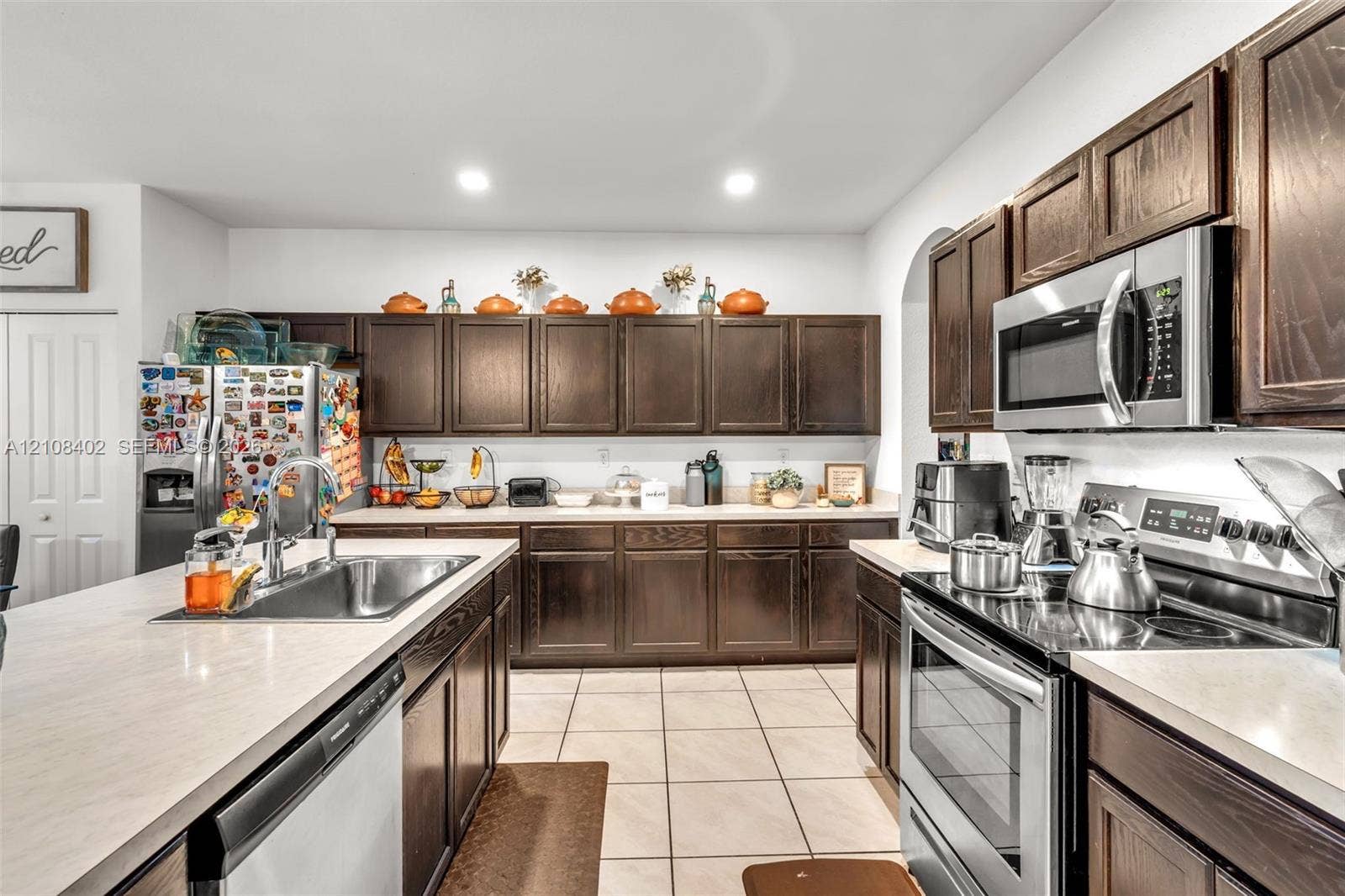 11771 SW 243rd Street, Homestead, FL 33032 Kitchen featuring dark wood cabinetry, stainless steel appliances, solid surface countertops, a stainless steel undermount sink, and tiled flooring