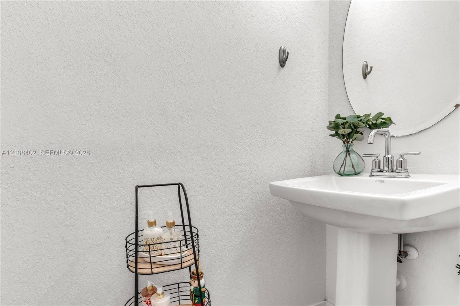 11771 SW 243rd Street, Homestead, FL 33032 Pedestal sink featuring a polished chrome faucet and a circular wall-mounted mirror