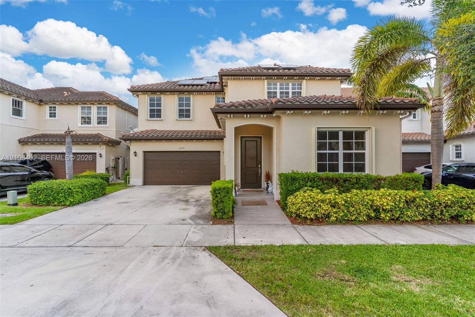 11771 SW 243rd Street, Homestead, FL 33032 Stucco exterior featuring a clay tile roof, arched entryway, multi-panel garage door, and solar panels
