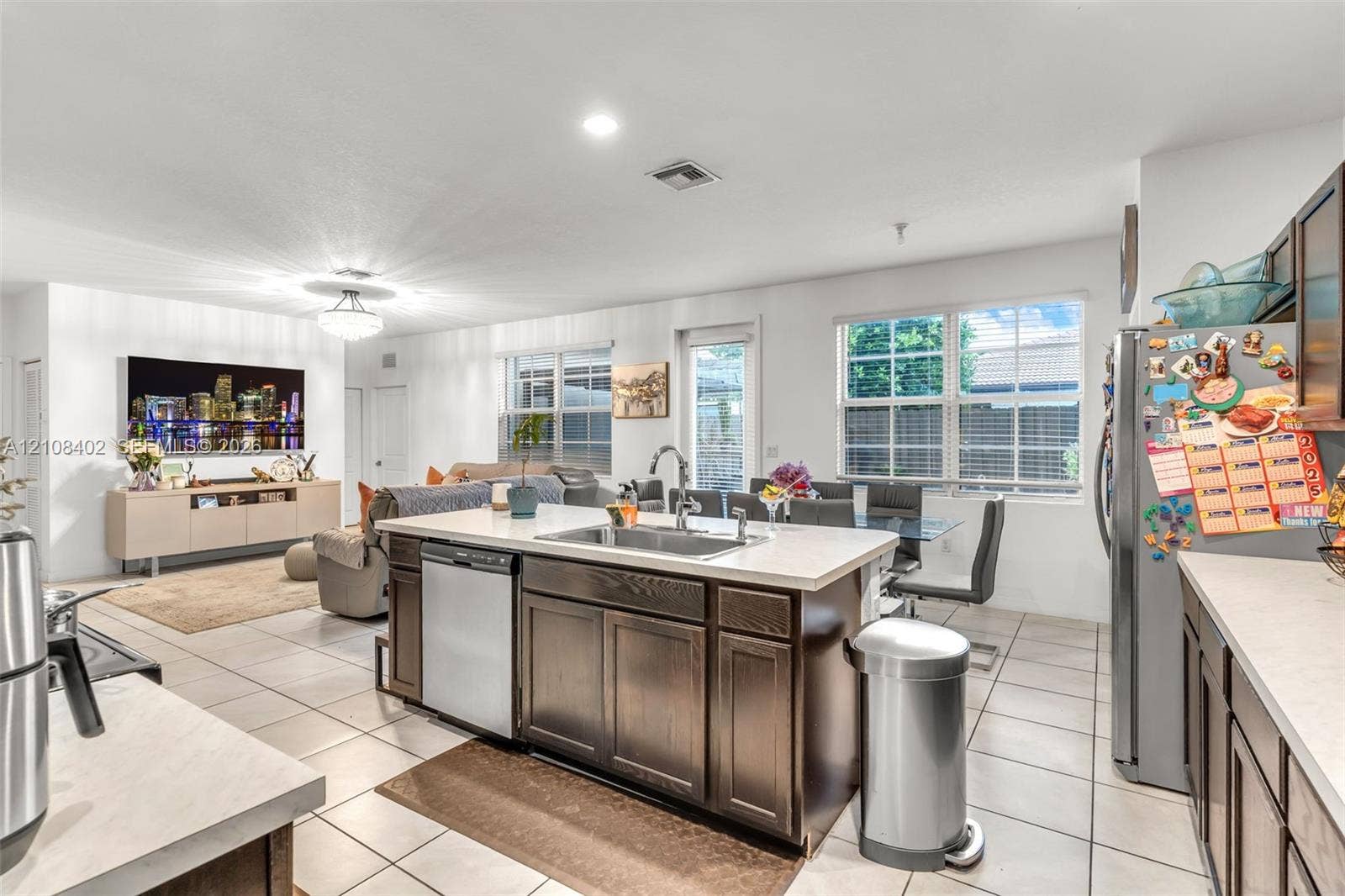 11771 SW 243rd Street, Homestead, FL 33032 Kitchen featuring a central island with a stainless steel undermount sink, dark wood-finish cabinetry, solid-surface countertops, tile flooring, and stainless steel appliances