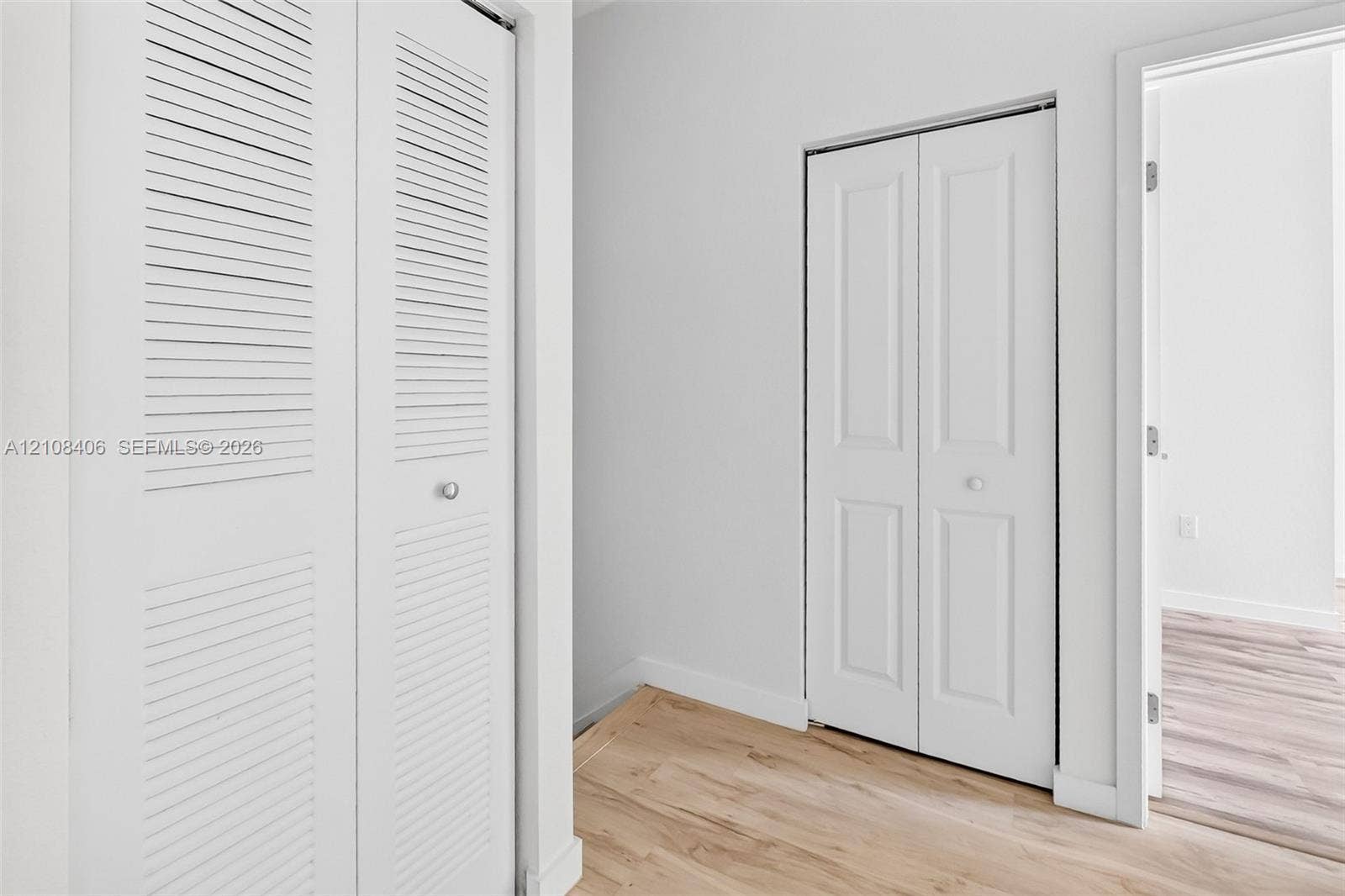 15650 SW 136th Street, #212, Miami, FL 33196 White bi-fold doors with louvered panels, white paneled doors, and light-toned wood-finish flooring