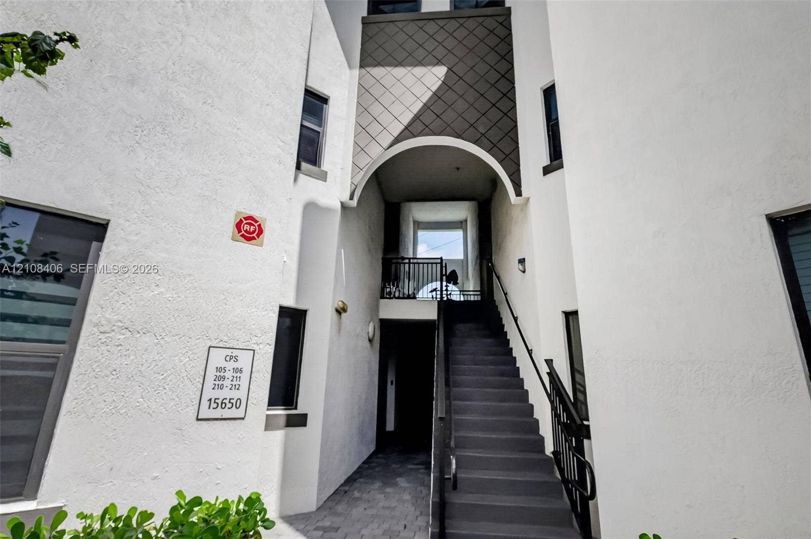 15650 SW 136th Street, #212, Miami, FL 33196 Stucco exterior featuring an arched entryway, diamond-patterned siding accents, and a metal staircase with a black handrail