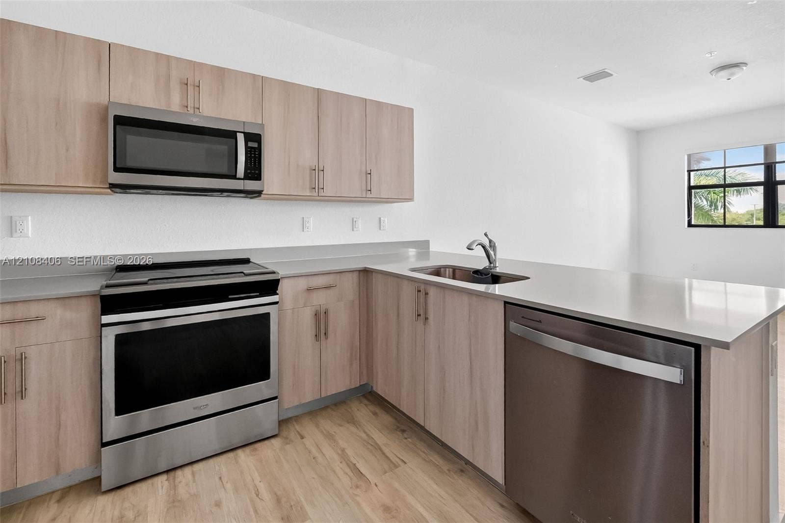 15650 SW 136th Street, #212, Miami, FL 33196 Kitchen featuring light-tone flat-panel cabinetry, stainless steel appliances, solid-surface countertops, an undermount sink with a pull-down faucet, and wood-finish flooring