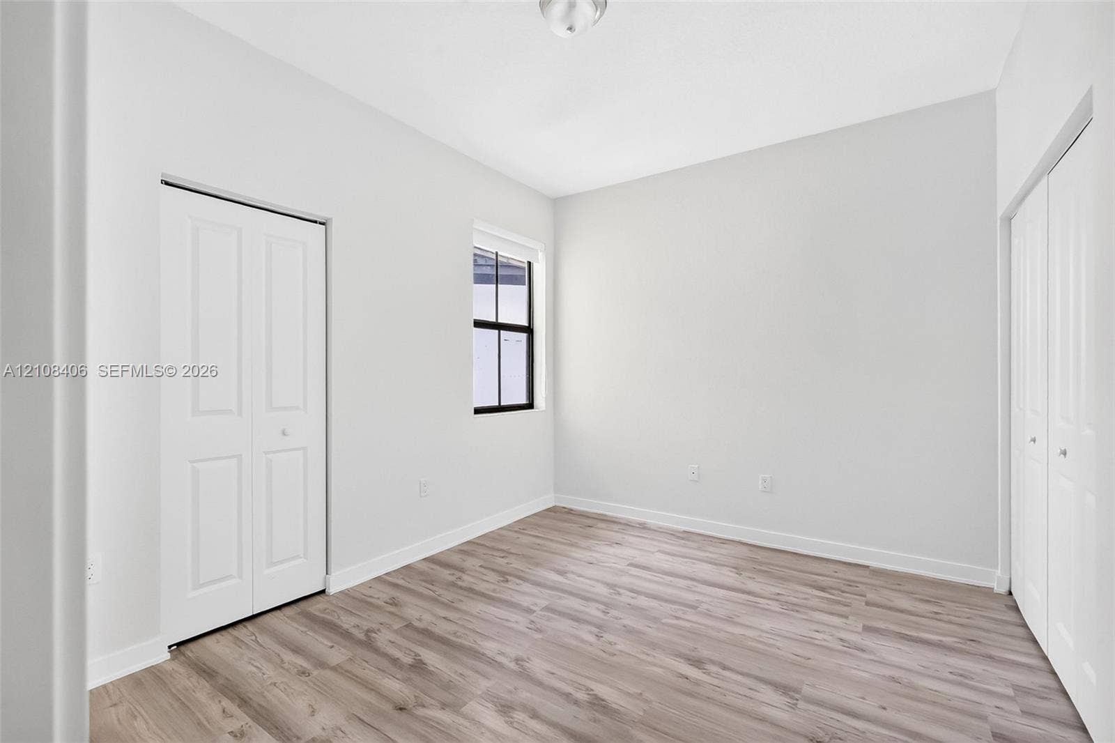 15650 SW 136th Street, #212, Miami, FL 33196 Neutral interior featuring wood-finish flooring, two sets of white paneled bi-fold closet doors, and a window with a black frame