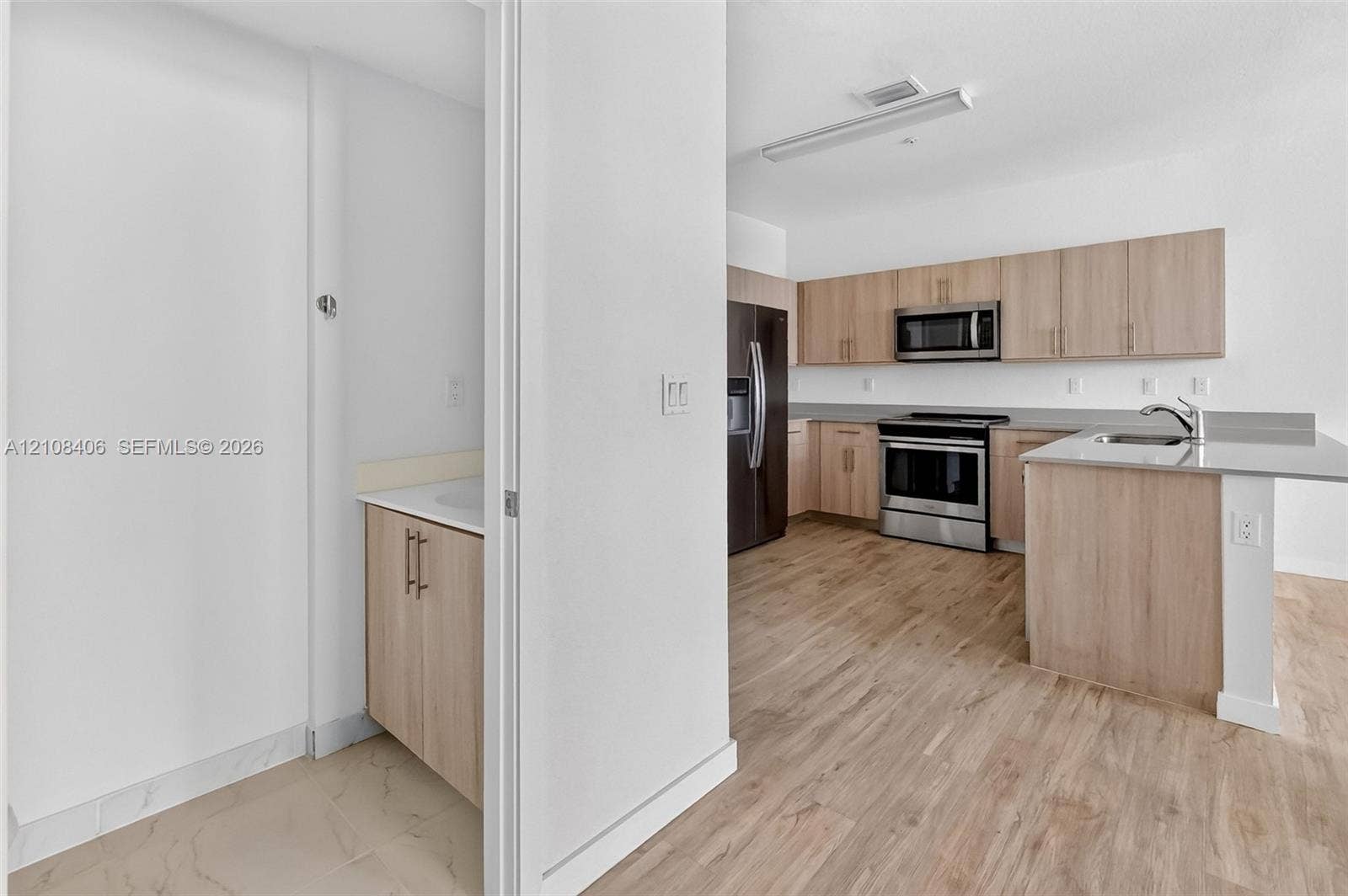 15650 SW 136th Street, #212, Miami, FL 33196 Kitchen featuring light-finish cabinetry, stainless steel appliances, and a peninsula with a stone-surface countertop, complemented by wood-finish flooring throughout