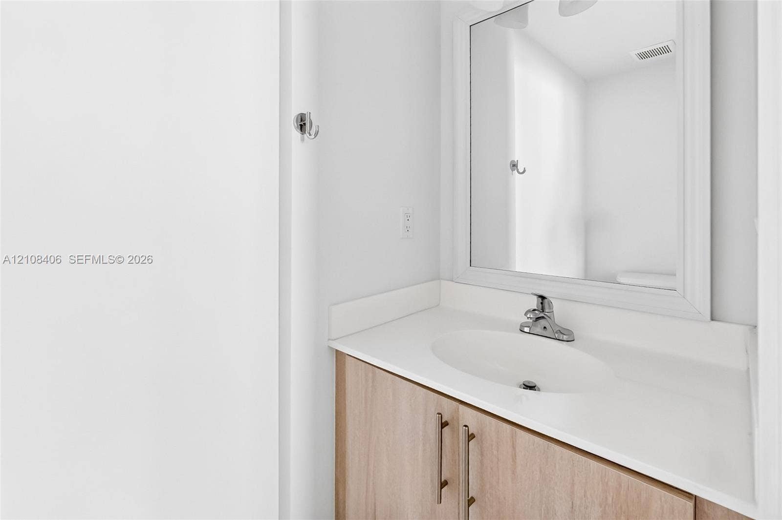 15650 SW 136th Street, #212, Miami, FL 33196 Wood-finish vanity cabinet with metallic hardware, integrated white countertop, oval basin, and a framed mirror