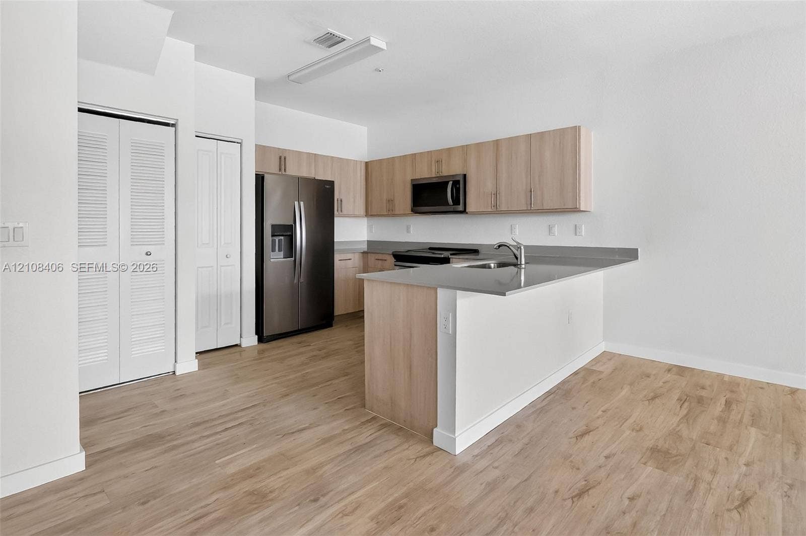 15650 SW 136th Street, #212, Miami, FL 33196 Kitchen featuring light wood-finish cabinetry, solid surface countertops, stainless steel appliances, and wood-finish flooring