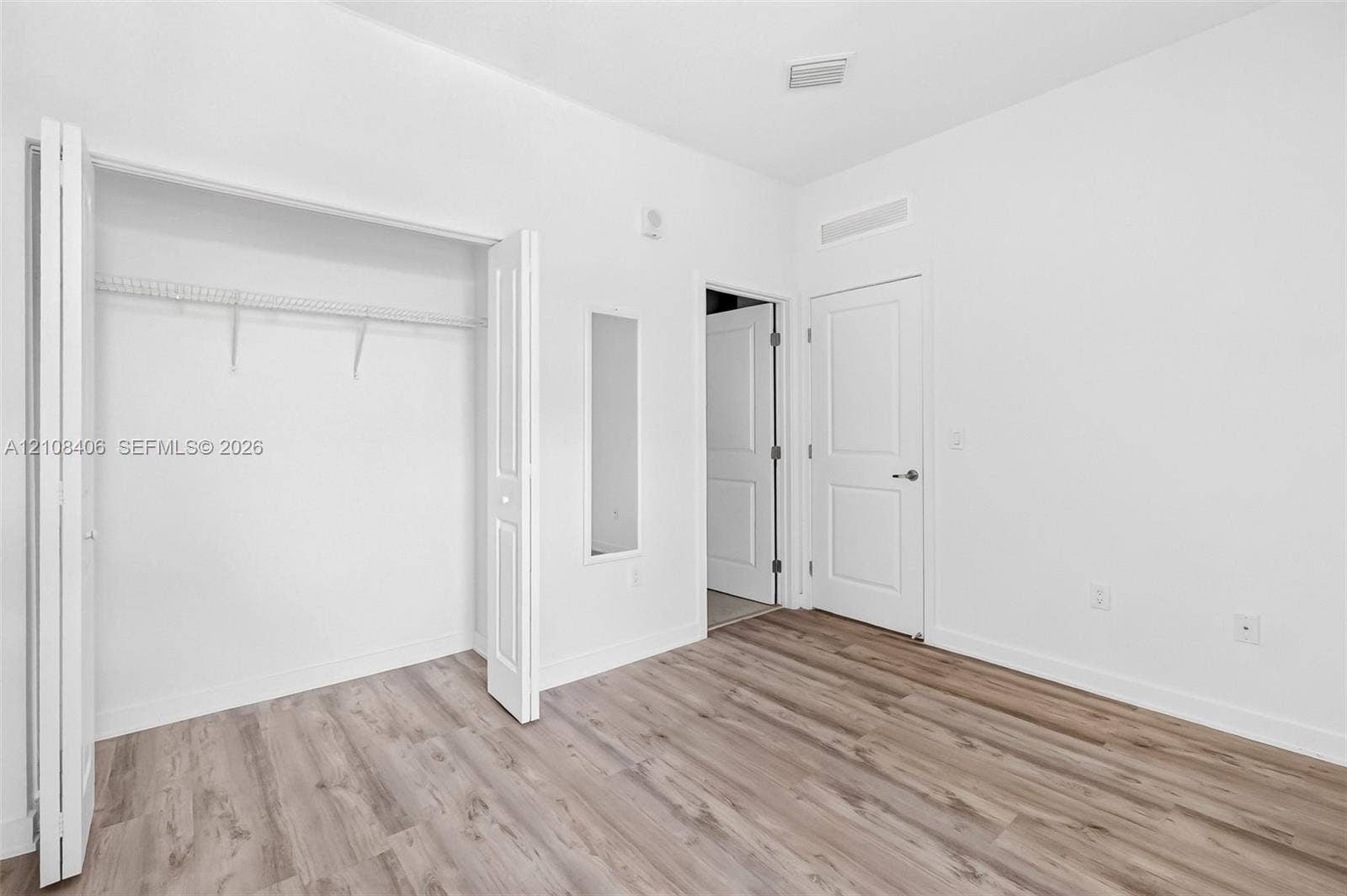 15650 SW 136th Street, #212, Miami, FL 33196 Room featuring wood-finish flooring, a bi-fold closet with built-in wire shelving, and a panel door