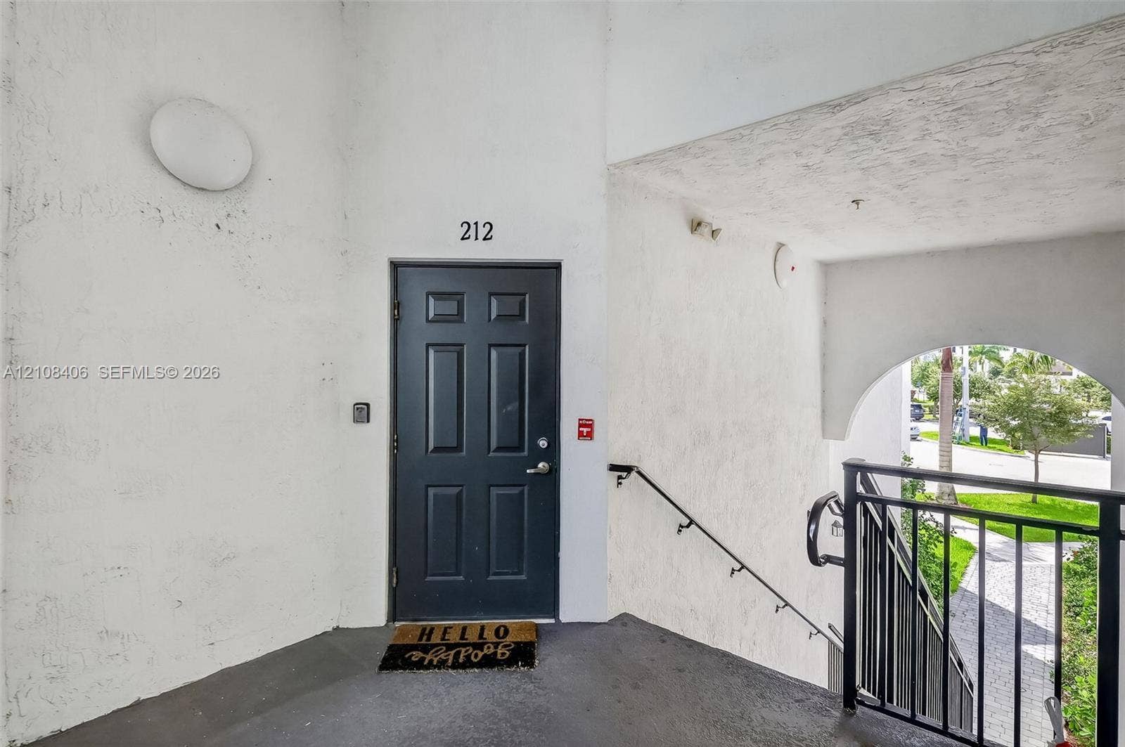 15650 SW 136th Street, #212, Miami, FL 33196 Exterior entry featuring a dark-toned paneled door, textured wall finish, and an arched entryway with a black metal railing