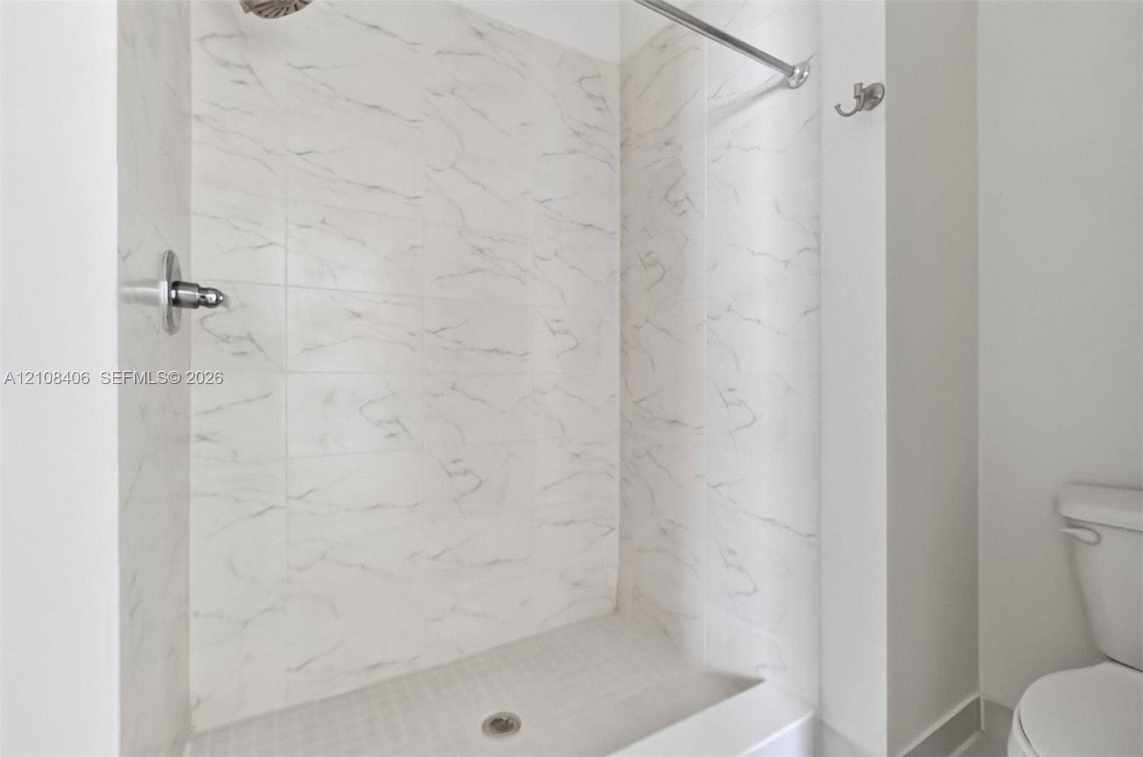 15650 SW 136th Street, #212, Miami, FL 33196 Shower enclosure featuring white tile with grey veining, a wall-mounted shower head, a chrome shower valve, a metal shower curtain rod, and a wall-mounted hook
