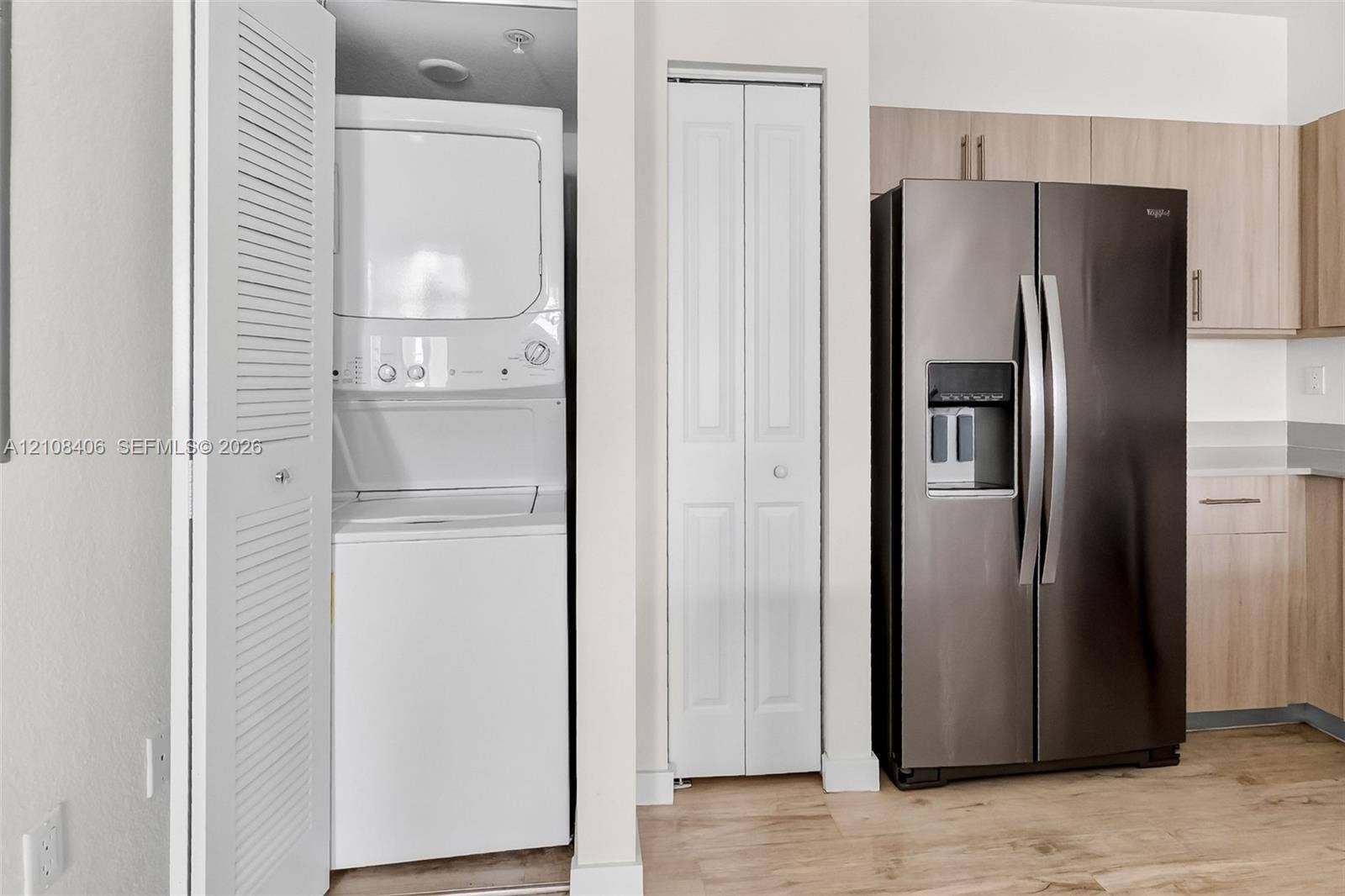 15650 SW 136th Street, #212, Miami, FL 33196 Built-in laundry closet with stacked washer and dryer, side-by-side stainless steel refrigerator, light-tone wood-finish cabinetry, and wood-finish flooring