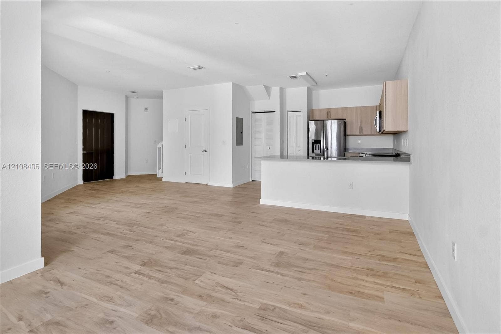 15650 SW 136th Street, #212, Miami, FL 33196 Open floor plan featuring wood-finish flooring, kitchen with light-tone cabinetry, stainless steel refrigerator, and a breakfast bar
